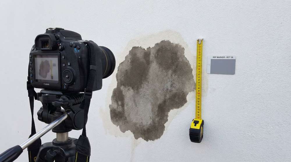 Professional camera documenting water damage on wall with reference marker and tape measure for insurance evidence
